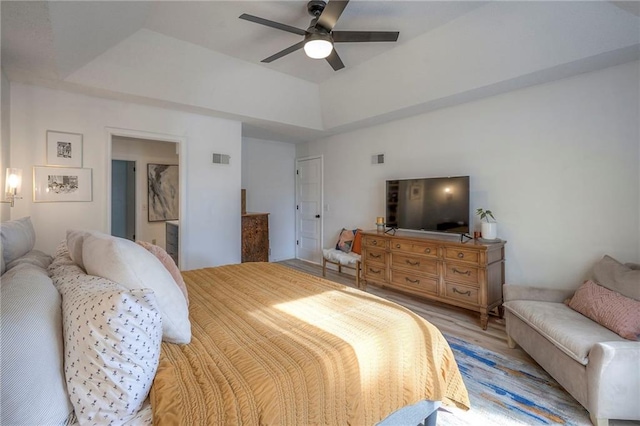 bedroom featuring light hardwood / wood-style floors, ceiling fan, and a tray ceiling