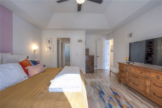 bedroom with ceiling fan, light wood-type flooring, and a tray ceiling