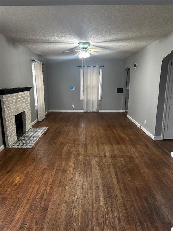 unfurnished living room with a textured ceiling, a fireplace, ceiling fan, and dark wood-type flooring