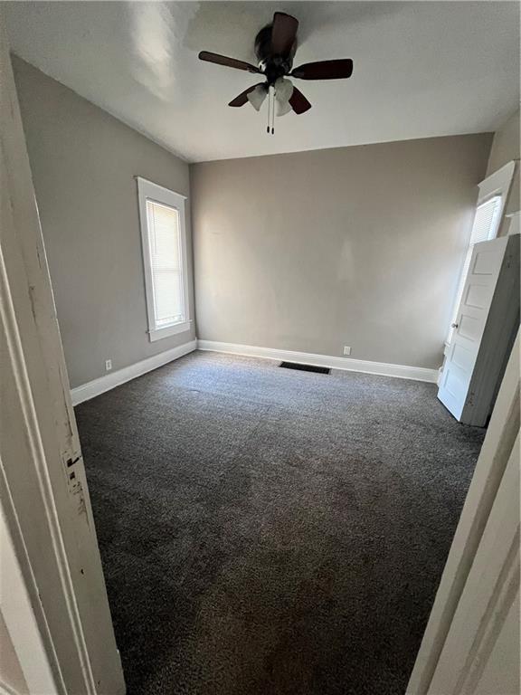 empty room featuring ceiling fan and dark carpet