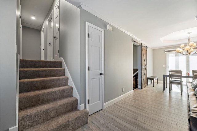 stairway with crown molding, a barn door, a chandelier, and hardwood / wood-style floors