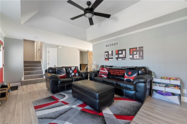 living room featuring crown molding, ceiling fan, a tray ceiling, wood-type flooring, and a barn door