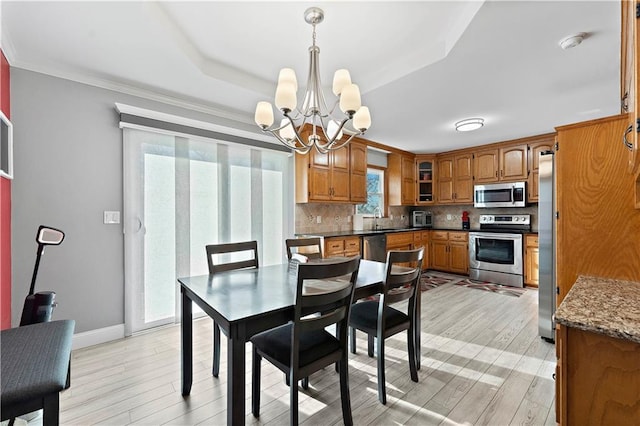 dining room featuring sink, a tray ceiling, a chandelier, and light wood-type flooring