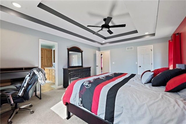 carpeted bedroom with ensuite bath, a raised ceiling, and ceiling fan