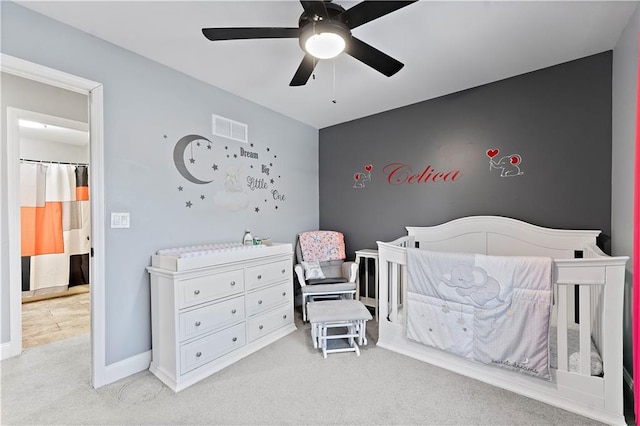 carpeted bedroom featuring a nursery area and ceiling fan