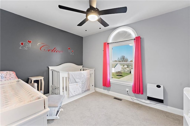 carpeted bedroom with a nursery area, ceiling fan, and heating unit