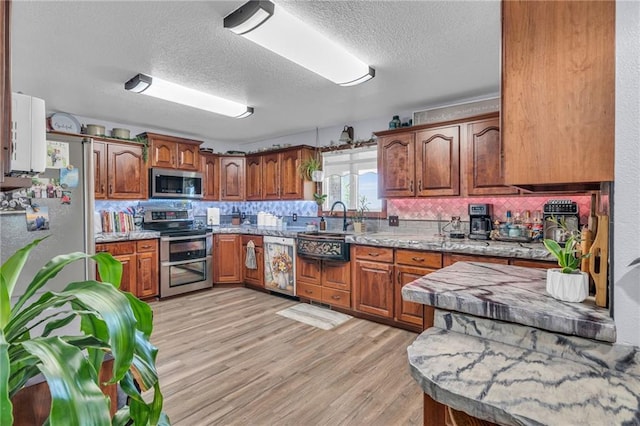 kitchen with backsplash, light hardwood / wood-style flooring, light stone countertops, a textured ceiling, and stainless steel appliances