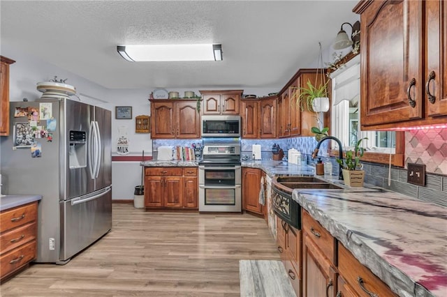 kitchen featuring sink, backsplash, light hardwood / wood-style floors, a textured ceiling, and appliances with stainless steel finishes