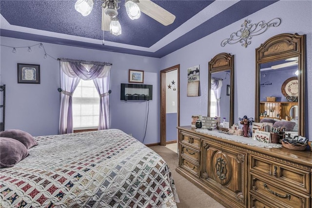 bedroom with a textured ceiling, ceiling fan, light carpet, and a tray ceiling