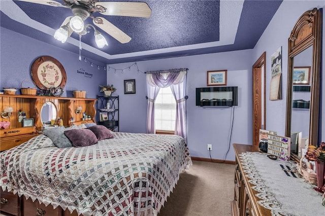 bedroom featuring a textured ceiling, carpet floors, a tray ceiling, and ceiling fan