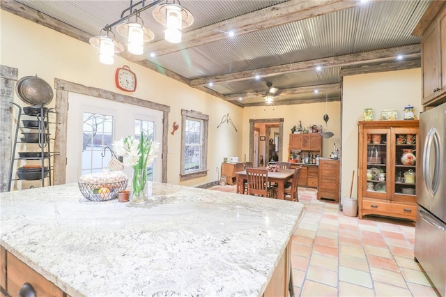 kitchen with hanging light fixtures, ceiling fan, stainless steel fridge, beamed ceiling, and a kitchen island