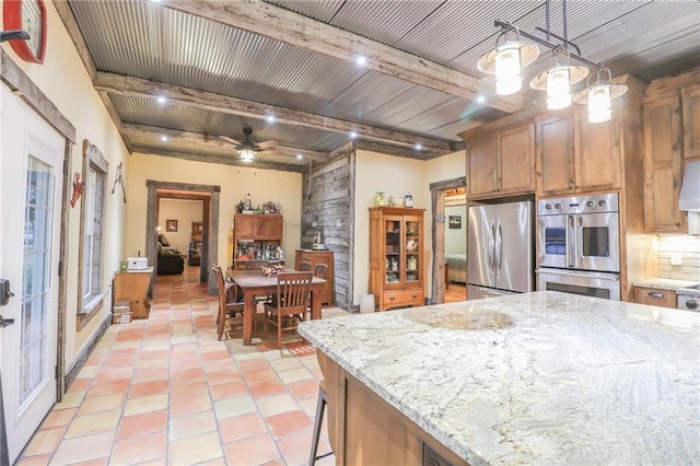 kitchen with pendant lighting, ceiling fan, beamed ceiling, light stone counters, and stainless steel appliances