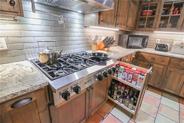 kitchen featuring stainless steel gas stovetop, backsplash, light stone countertops, light tile patterned floors, and custom range hood