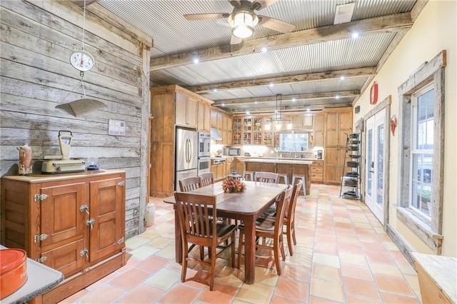 dining area with wood walls, beamed ceiling, light tile patterned floors, and ceiling fan