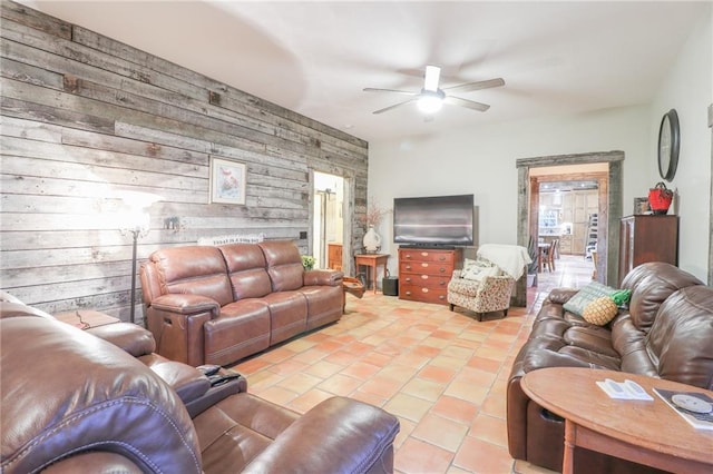 tiled living room featuring a wealth of natural light, wood walls, and ceiling fan