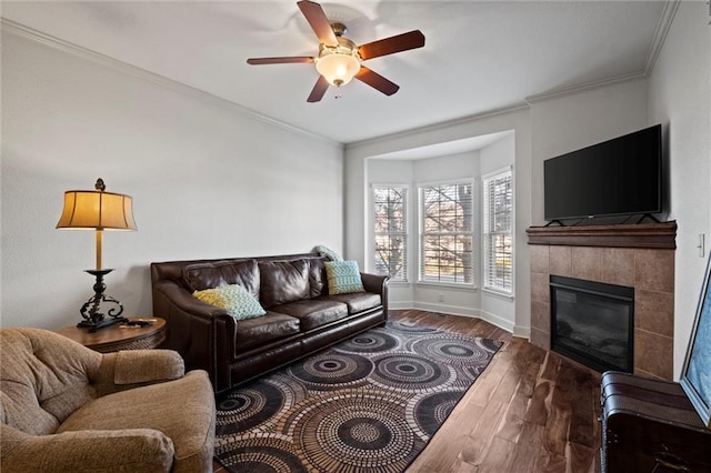 living room with dark hardwood / wood-style flooring, ceiling fan, crown molding, and a tiled fireplace