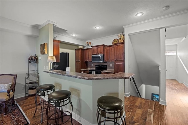 kitchen with black appliances, a kitchen breakfast bar, crown molding, dark hardwood / wood-style floors, and kitchen peninsula