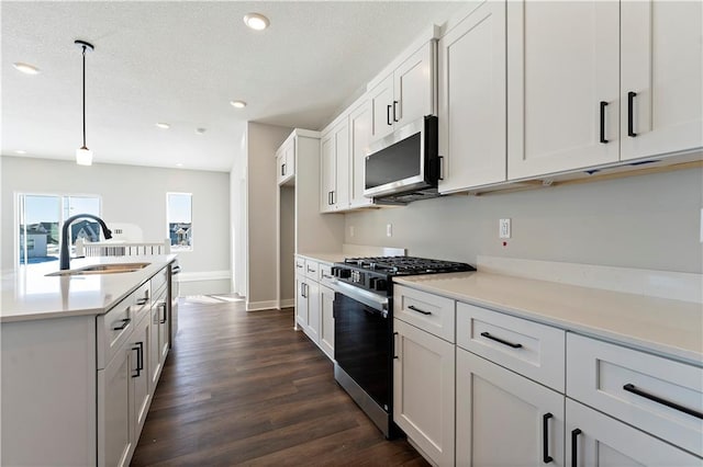 kitchen with dark wood-type flooring, sink, hanging light fixtures, appliances with stainless steel finishes, and white cabinets