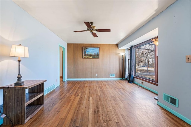 unfurnished living room featuring wooden walls, hardwood / wood-style floors, and ceiling fan