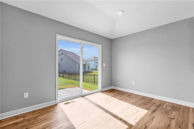 unfurnished room featuring lofted ceiling, wood finished floors, visible vents, and baseboards