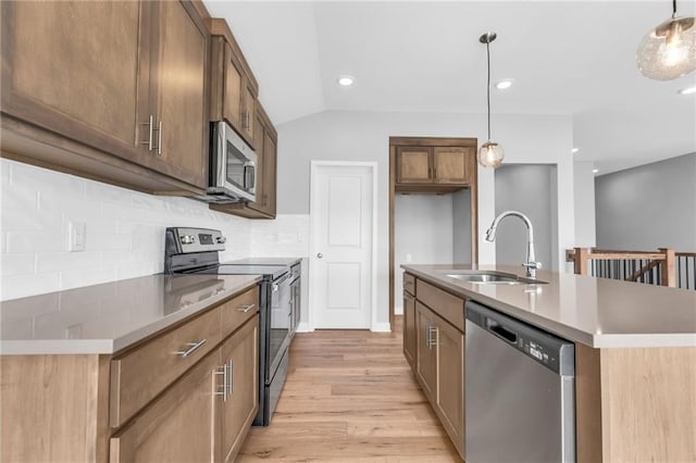 kitchen with tasteful backsplash, hanging light fixtures, light wood-style flooring, appliances with stainless steel finishes, and a sink