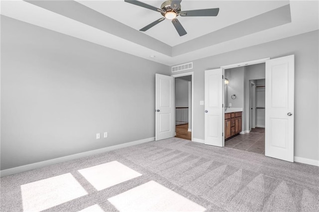 unfurnished bedroom with baseboards, visible vents, connected bathroom, a raised ceiling, and carpet flooring