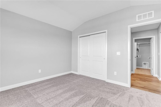 unfurnished bedroom featuring a closet, visible vents, carpet flooring, vaulted ceiling, and baseboards