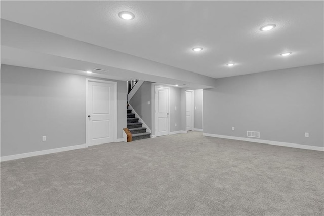 finished below grade area featuring carpet floors, baseboards, stairs, and visible vents