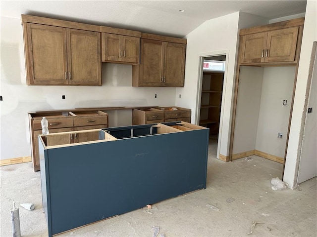 17756 Houston St, Gardner, KS 66030 - kitchen featuring a center island, lofted ceiling, baseboards, and brown cabinetry