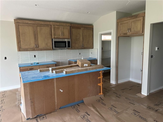 17756 Houston St, Gardner, KS 66030 - kitchen with stainless steel microwave, tasteful backsplash, lofted ceiling, brown cabinetry, and a center island