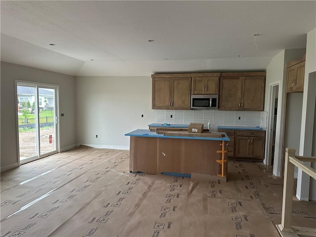 17756 Houston St, Gardner, KS 66030 - kitchen with stainless steel microwave, backsplash, a kitchen island, brown cabinets, and vaulted ceiling