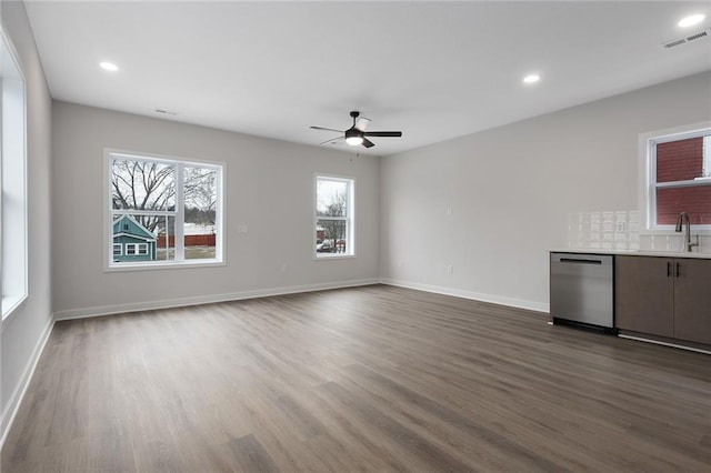 unfurnished living room with recessed lighting, dark wood-type flooring, a sink, visible vents, and baseboards