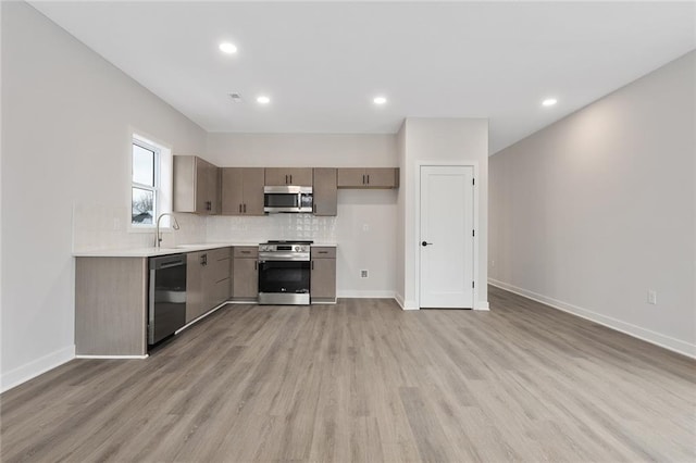 kitchen featuring light wood finished floors, decorative backsplash, stainless steel appliances, and light countertops