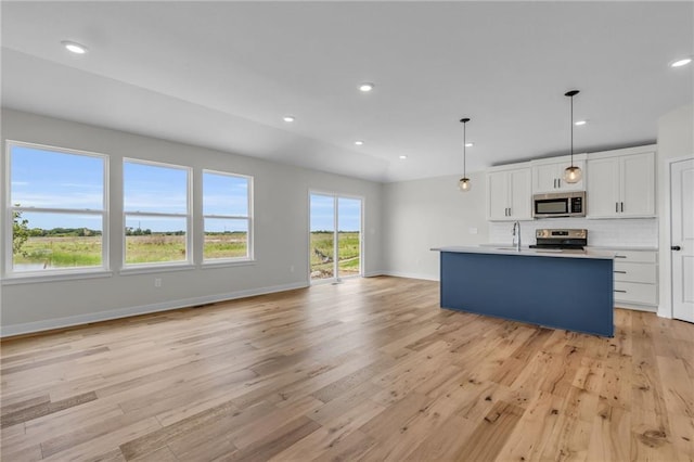 kitchen with decorative light fixtures, tasteful backsplash, white cabinets, a kitchen island with sink, and stainless steel appliances