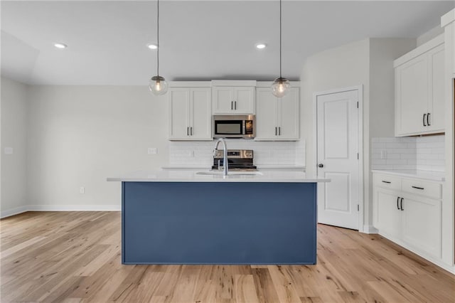 kitchen with a center island with sink, appliances with stainless steel finishes, hanging light fixtures, and white cabinets