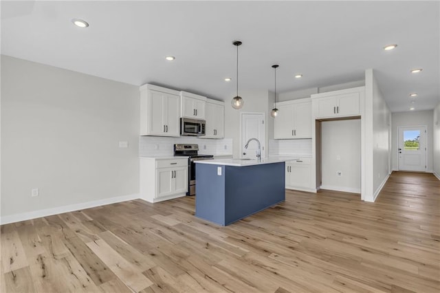 kitchen with appliances with stainless steel finishes, white cabinetry, a kitchen island with sink, tasteful backsplash, and decorative light fixtures