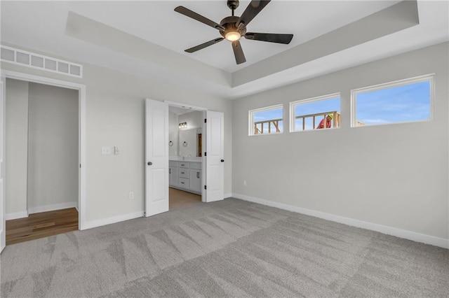 unfurnished bedroom featuring light carpet, a raised ceiling, ceiling fan, and ensuite bathroom