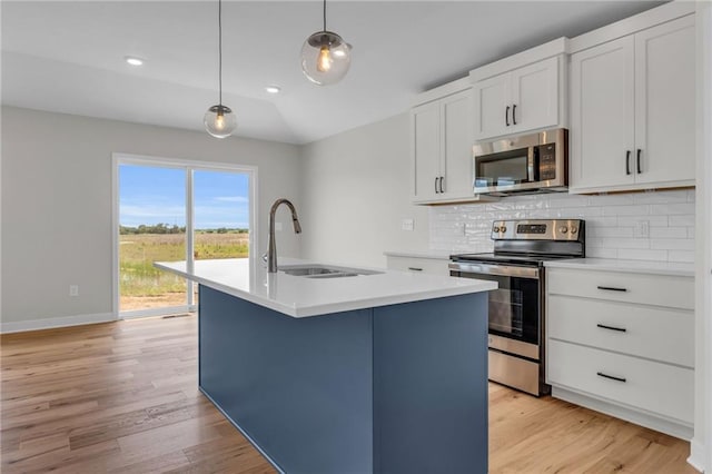 kitchen featuring decorative backsplash, appliances with stainless steel finishes, a kitchen island with sink, light wood-style floors, and a sink