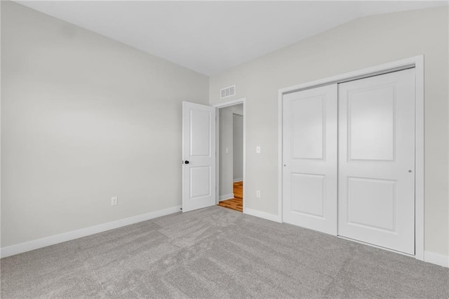 unfurnished bedroom with lofted ceiling, carpet floors, visible vents, baseboards, and a closet