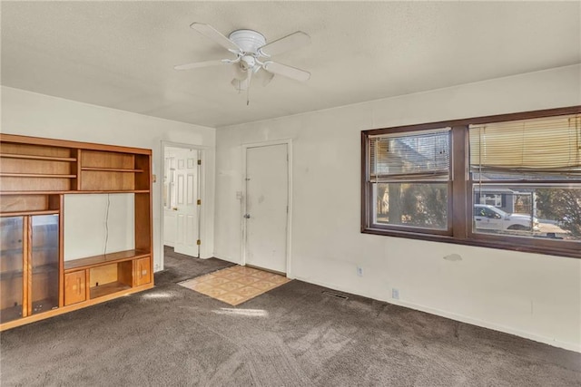 unfurnished living room with ceiling fan and dark carpet