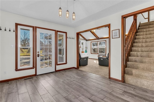 doorway with a textured ceiling, light hardwood / wood-style floors, and vaulted ceiling