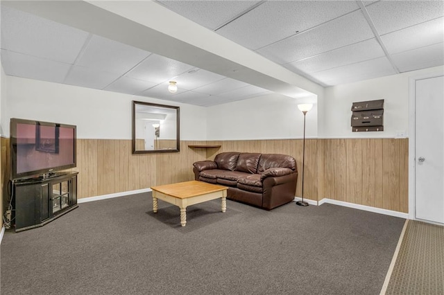 carpeted living room featuring a drop ceiling and wooden walls