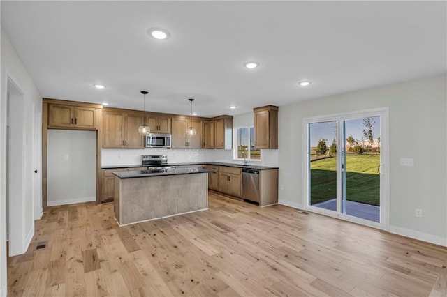 kitchen with appliances with stainless steel finishes, decorative light fixtures, a kitchen island, and light wood-type flooring