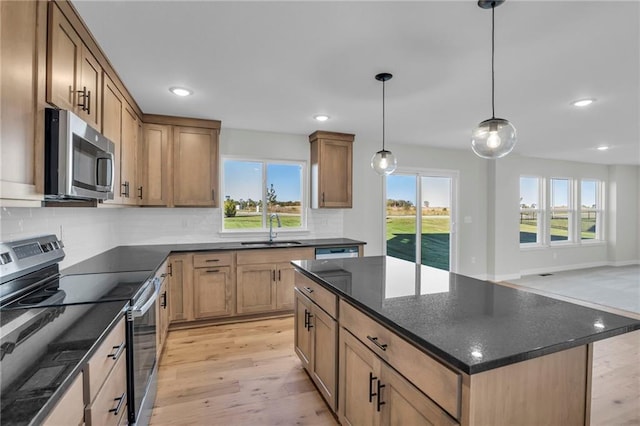 kitchen with appliances with stainless steel finishes, sink, hanging light fixtures, a center island, and light hardwood / wood-style flooring