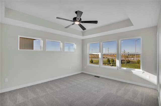 empty room with ceiling fan, a raised ceiling, and carpet floors