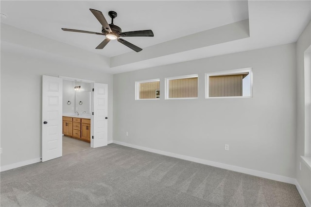 unfurnished bedroom with light carpet, connected bathroom, a tray ceiling, and ceiling fan