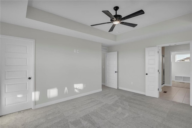 unfurnished bedroom with light colored carpet, ceiling fan, and a tray ceiling