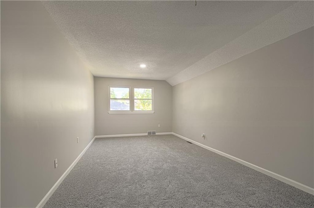 spare room with a textured ceiling, carpet flooring, and lofted ceiling