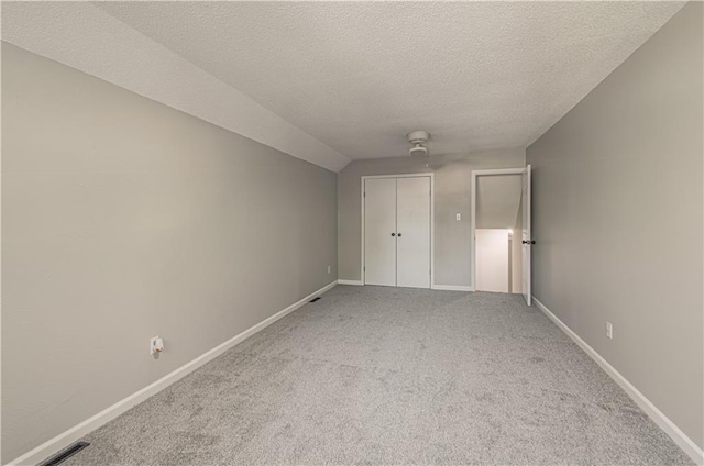 unfurnished bedroom featuring lofted ceiling, ceiling fan, a textured ceiling, carpet floors, and a closet