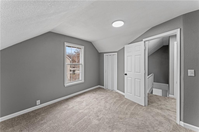 additional living space with lofted ceiling, a textured ceiling, and light carpet